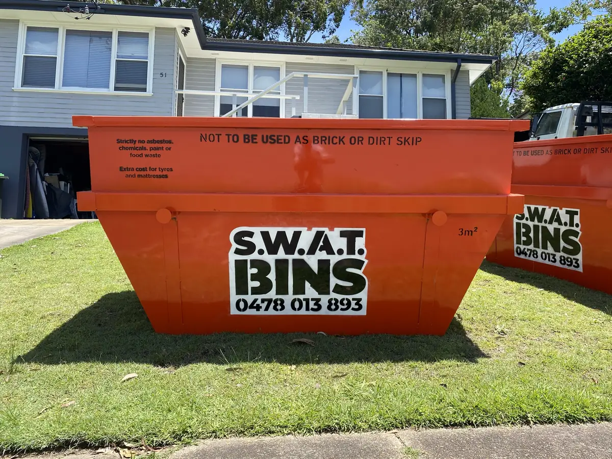 Two orange SWAT Bins skip bins sitting on the front lawn of a weatherboard house