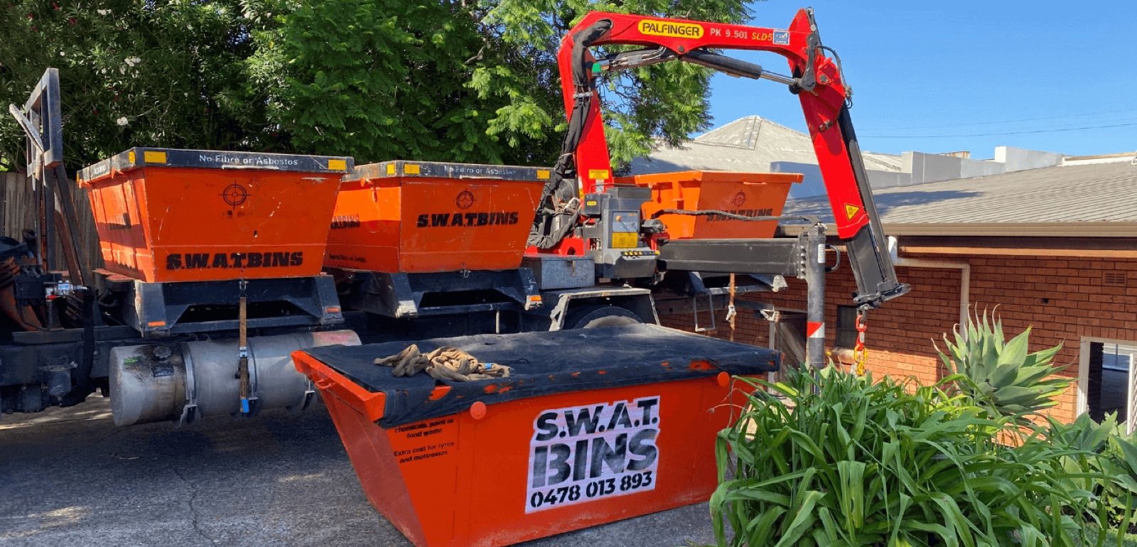 The SWAT Bins custom crane truck swapping orange skip bins on a Newcastle driveway
