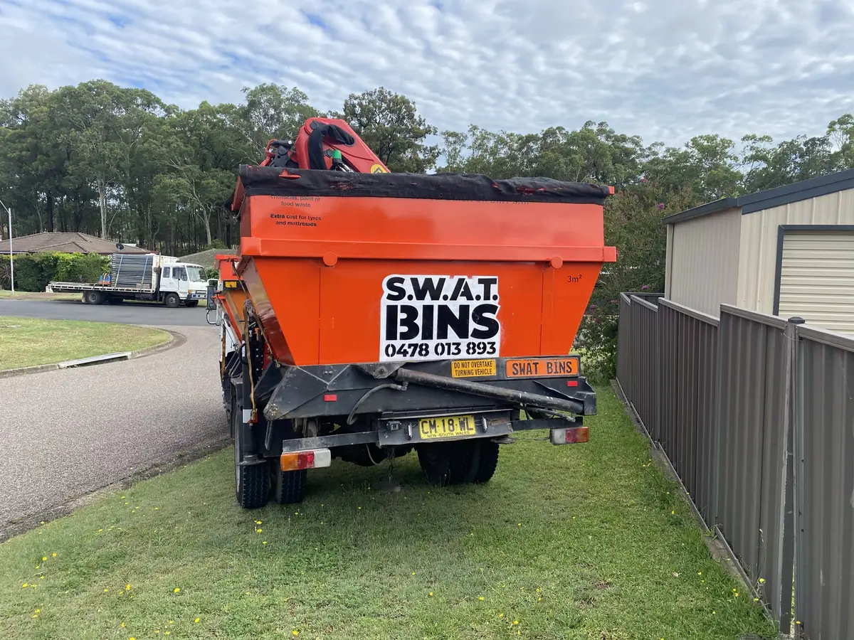 The SWAT Bins crane truck, loaded with orange skip bins, parked on a suburban street